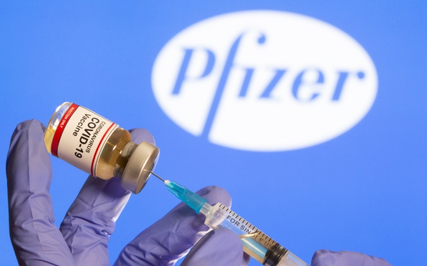 A woman holds a small bottle labeled with a "Coronavirus COVID-19 Vaccine" sticker and a medical syringe in front of displayed Pfizer logo in this illustration taken, October 30, 2020. REUTERS/Dado Ruvic