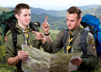 Two young scout boys with backpacks holding the map and showing the right way traveling in the mountains