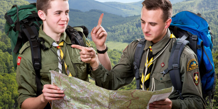 Two young scout boys with backpacks holding the map and showing the right way traveling in the mountains